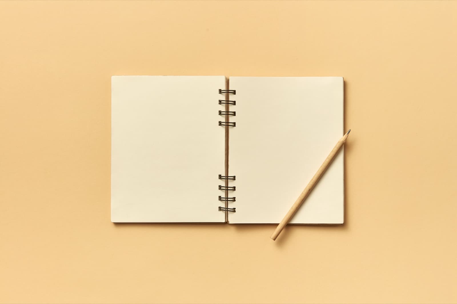 Cuaderno de notas abierto en blanco con un lápiz, sobre un fondo beige liso